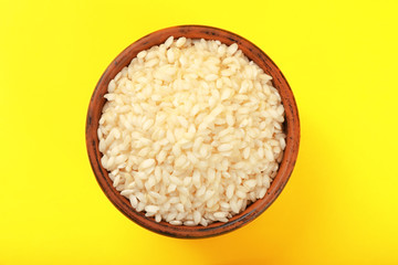 Bowl with raw rice on color background