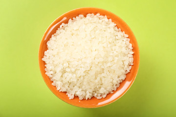 Bowl with raw rice on color background