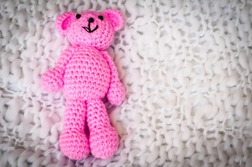 A soft pink teddy bear, toy for infant girl, isolated on a white blanket background. Sudden infant...