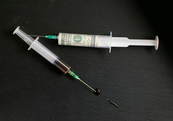 The concept of money and drugs. Money in one syringe and a drug in another on a dark background.