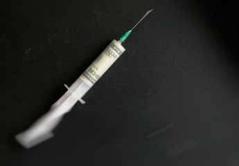 The concept of money and drugs. A hundred dollars in a syringe against a dark background. Blur effect.