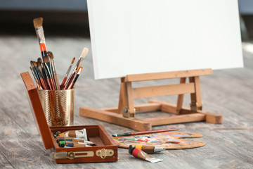 Set of brushes and paints with easel on floor in artist's workshop