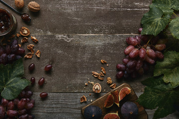 top view of sliced figs on cutting board, fresh ripe grapes, jam and walnuts on wooden table