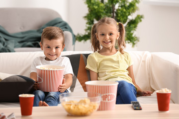 Cute children eating popcorn while watching TV at home