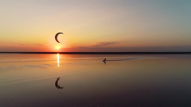 Man contols an orange training kite, sunset on the lake. Slow motion