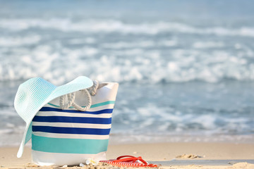 Beach bag with hat and flip-flops on sand near sea