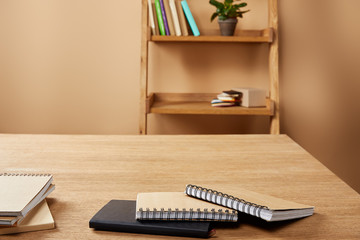 notebooks on wooden table, shelves with books and plant at home