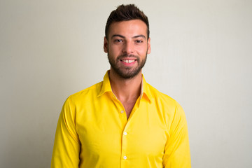 Studio shot of young handsome bearded businessman wearing yellow shirt