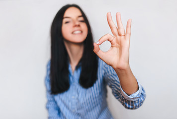 Beautiful young happy smiling girl in blue shirt showing ok sing with her hand. OK concept. Isolate. Copy space.