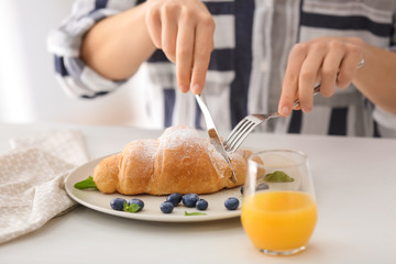 Woman eating tasty croissant at table