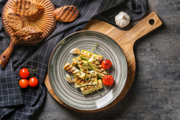 Plate with tasty grilled zucchini on wooden board