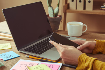 cropped image of girl holding smartphone with blank screen at table with laptop and stickers