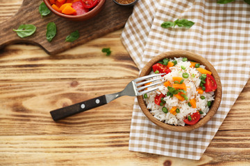 Bowl with tasty boiled rice and vegetables on wooden table