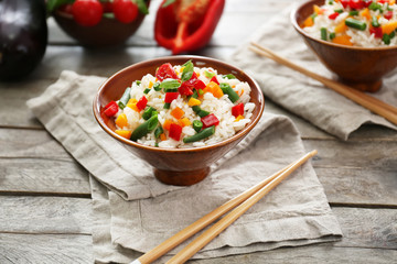 Bowl with tasty boiled rice and vegetables on wooden table
