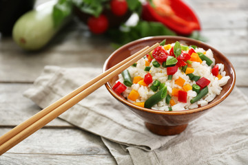 Bowl with tasty boiled rice and vegetables on wooden table