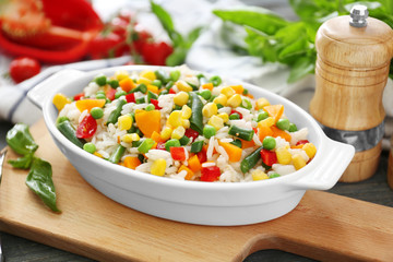 Dish with tasty boiled rice and vegetables on wooden board