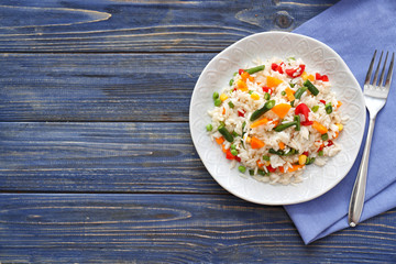 Plate with tasty boiled rice and vegetables on wooden table