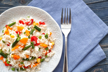 Plate with tasty boiled rice and vegetables on wooden table
