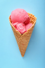Waffle cone with delicious strawberry ice-cream on color background