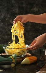 Woman holding fresh zucchini spaghetti over bowl