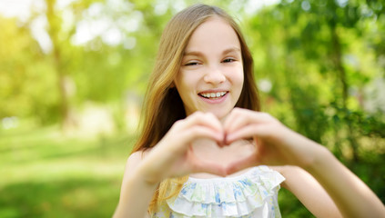 Cute preteen girl laughing and holding her hands in a heart shape on bright and sunny summer day....