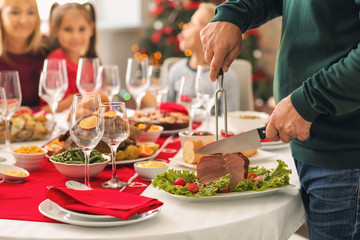 Obraz na płótnie Canvas Man cutting tasty ham during Christmas dinner