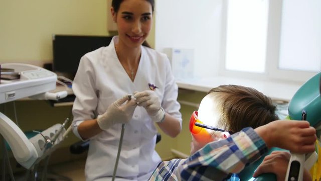 A young woman dentist is preparing for the treatment of teeth. The patient boy and his twin brother are smiling and having fun.