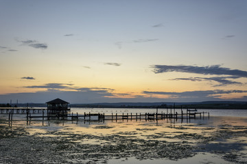 wooden Fishing hut in a lake with pier and fishing net at sunset.