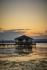 wooden Fishing hut in a lake with pier and fishing net at sunset.