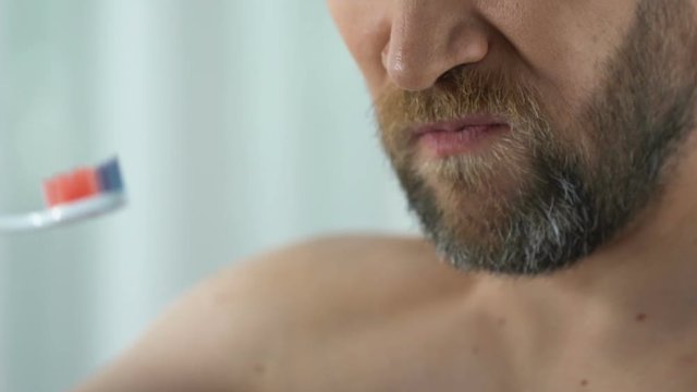 Bearded man feels tooth pain while cleaning teeth, showing toothbrush with blood