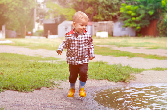 The little boy runs around in puddles in yellow rubber boots and a checkered raincoat.