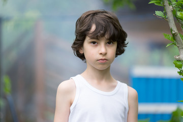 Portrait of a boy in a sleeveless shirt on a nature background. Country style.