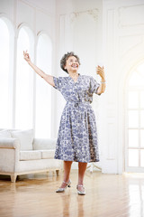 Asian grandmother with headphones listening to music, holding mobile phone in hand, happy to dance indoors