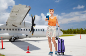 tourism, summer holidays and vacation concept - happy teenage girl in sunglasses with travel bag and air ticket over plane on airfield background