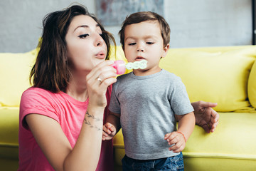 happy mom and little son blowing soap bubbles together at home