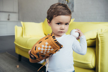 cute toddler playing with baseball glove and ball at home