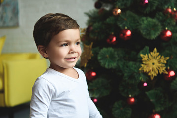 smiling little boy standing near christmas tree at home