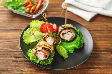Plate with tasty zucchini rolls on wooden table