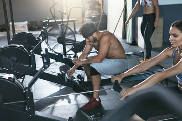 Fototapeta na wymiar Crossfit. People Exercising On Rowing Machine In Training Gym