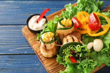 Tasty zucchini rolls with vegetables on wooden board
