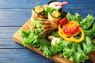 Tasty zucchini rolls with vegetables on wooden board