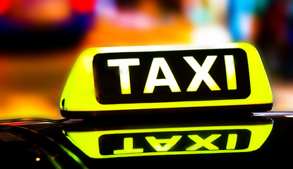 Night picture of a taxi car. Taxi sign on the car roof glowing in the dark