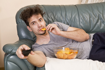 Man with remote and chips watching TV at home