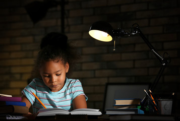 Little African-American girl doing homework in evening at home - obrazy, fototapety, plakaty