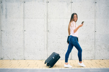 Woman carrying luggage and using smart phone while walking to the station.