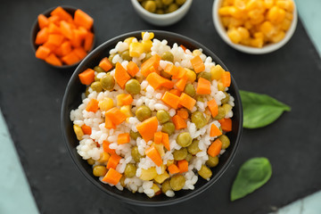 Bowl with tasty boiled rice and vegetables on slate plate, top view
