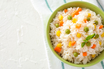 Bowl with tasty boiled rice and vegetables on white table