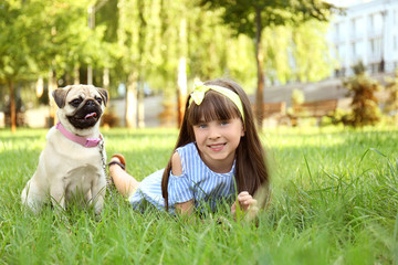 Cute little girl with pug dog in park on summer day
