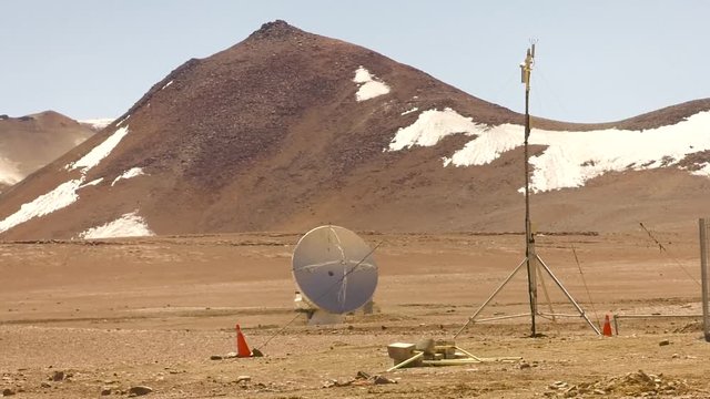 A wide shot of a small telescope at the alma observatory, with the Andes mountains behind it.