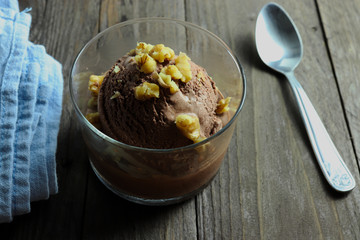 Chocolate ice cream with walnuts on wooden surface, dark moody photo